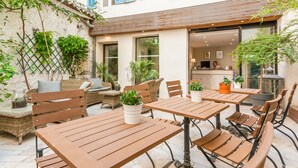 An outdoor patio area with wooden tables and wicker furniture, surrounded by potted plants and a stone wall. - Central Hotel (Avignon)