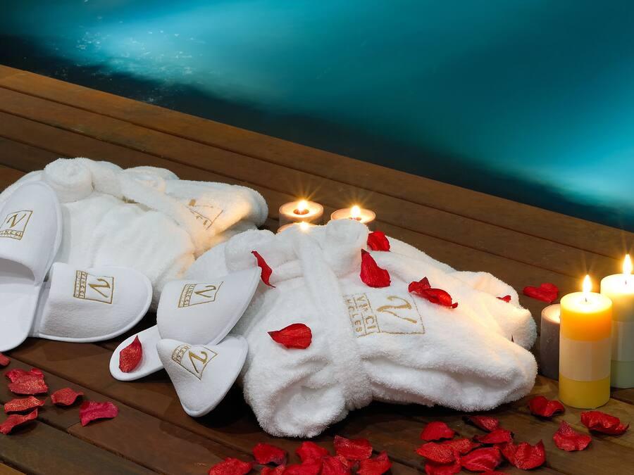 A wooden deck with white towels, slippers, and red rose petals, along with two lit candles.