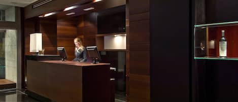 A reception desk with a dark wood finish, two computer monitors, and a glass display case with a bottle.