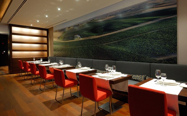 A restaurant with a long table and red chairs, a large wall mural of a vineyard, and a modern interior design.