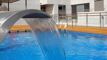 A swimming pool with a water feature, surrounded by a modern building with multiple windows and balconies.