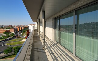 A balcony with a city view, large windows, and a clear sky.