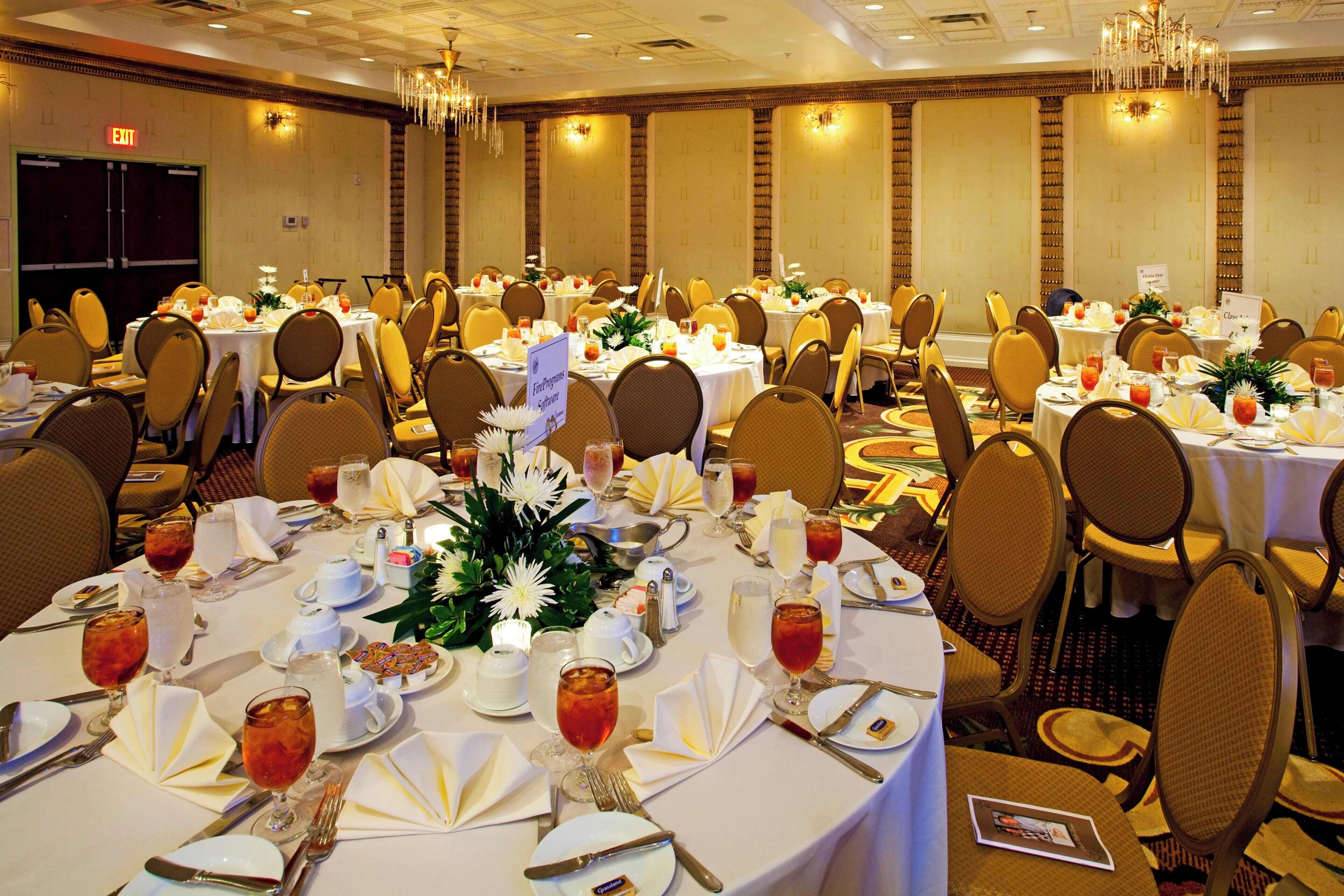 A banquet hall with round tables set for dining, chairs, and chandeliers.