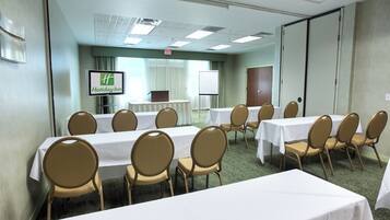A conference room with multiple tables and chairs, a screen displaying the Holiday Inn logo, and a whiteboard in the background.