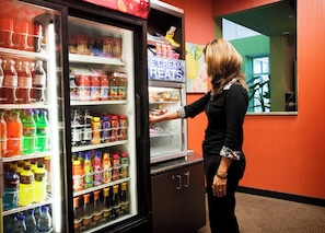 A person reaching into a refrigerated beverage display in a room with orange walls and a mirror reflecting the interior.