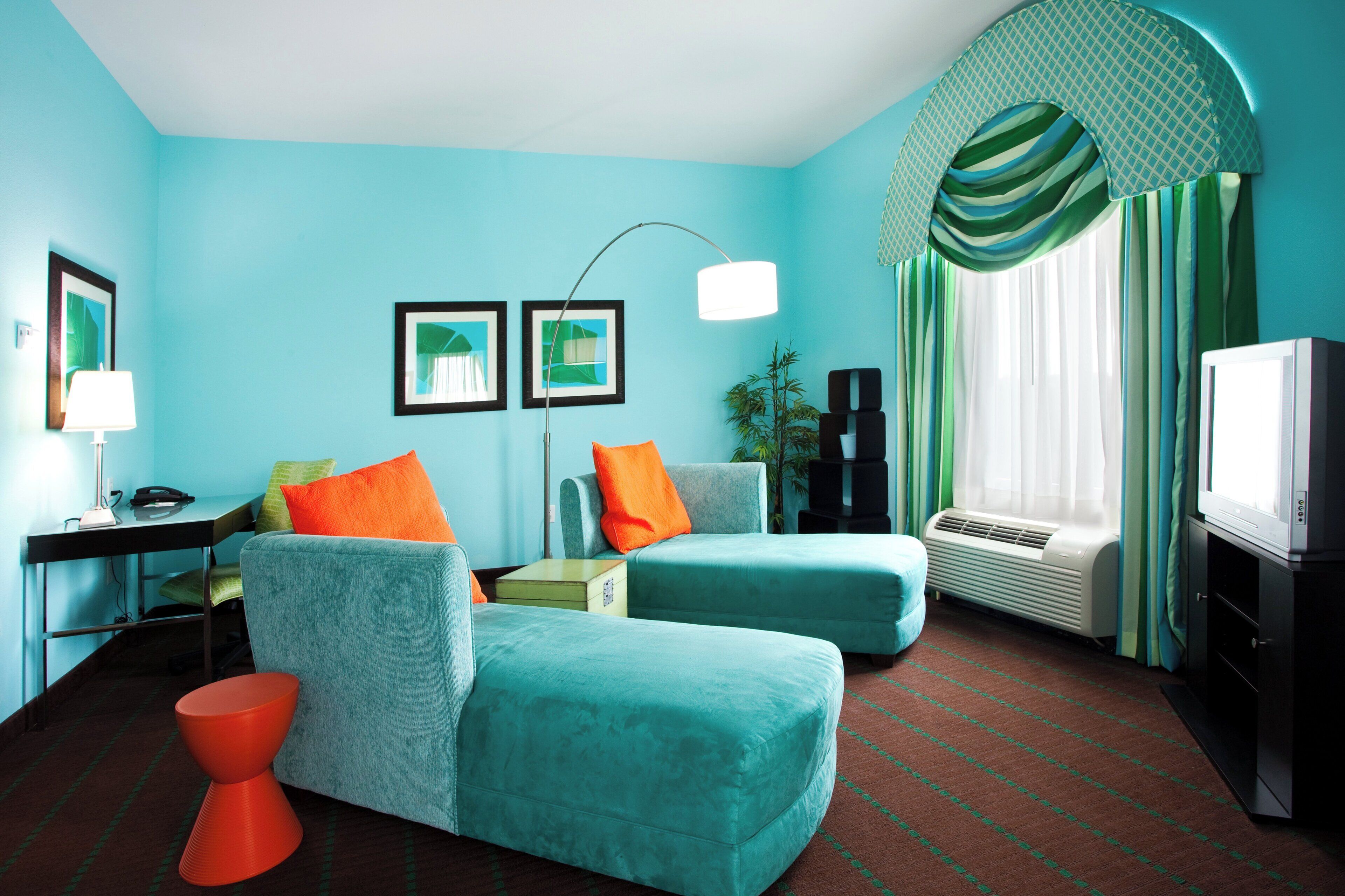 A room with teal walls, a sofa, a chair, a small table, a lamp, a television, and a window with curtains.