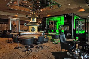 Un vaste espace salon avec un grand ensemble de sièges disposés au centre, un mur décoratif agrémenté d’une horloge et un bar illuminé de lumière verte.