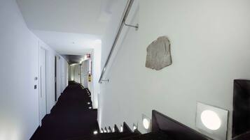 Ein Hotelkorridor mit Treppe, Handlauf und Wandleuchte.
