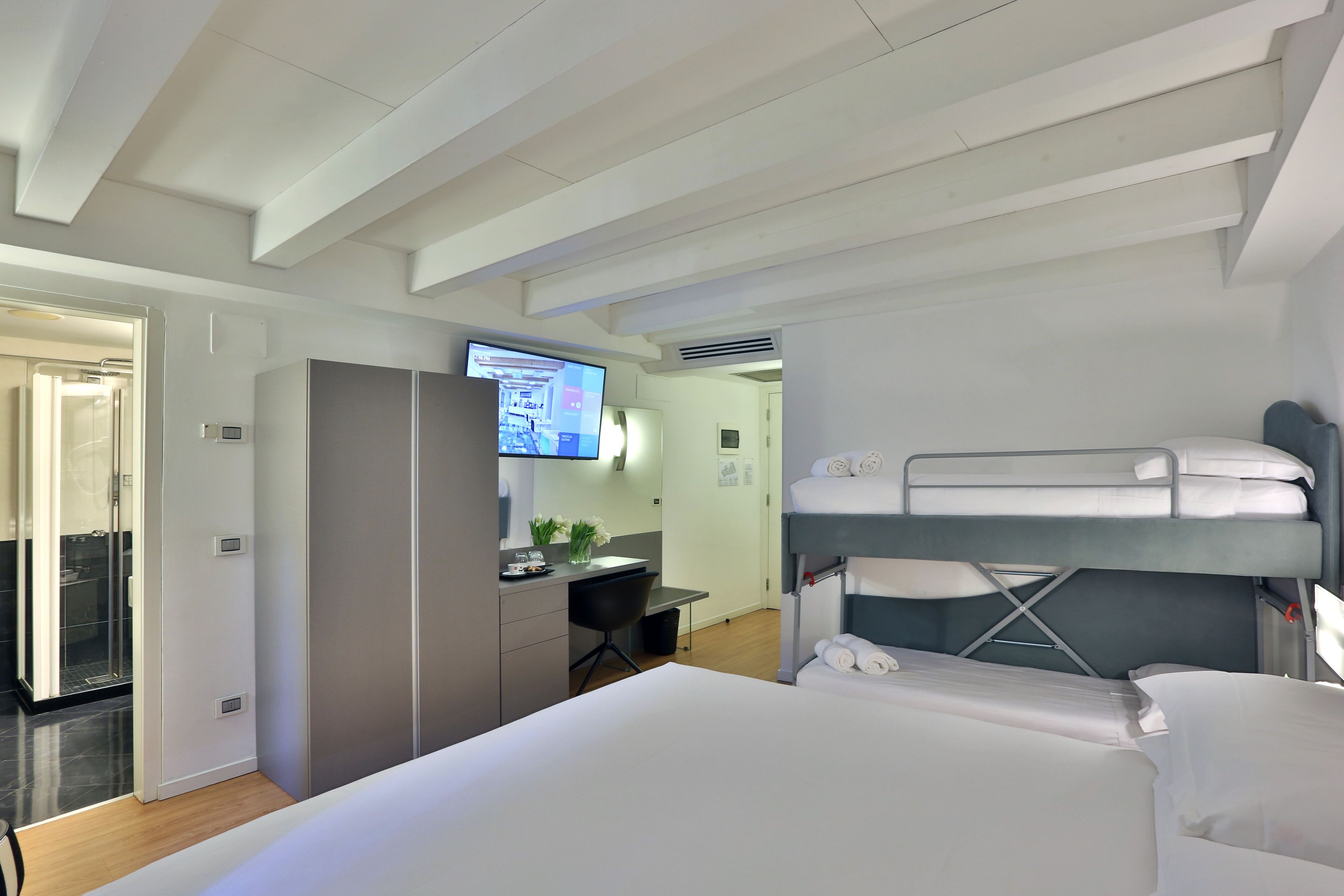 Una habitación de hotel moderna con una cama litera, un escritorio con computadora y un televisor.