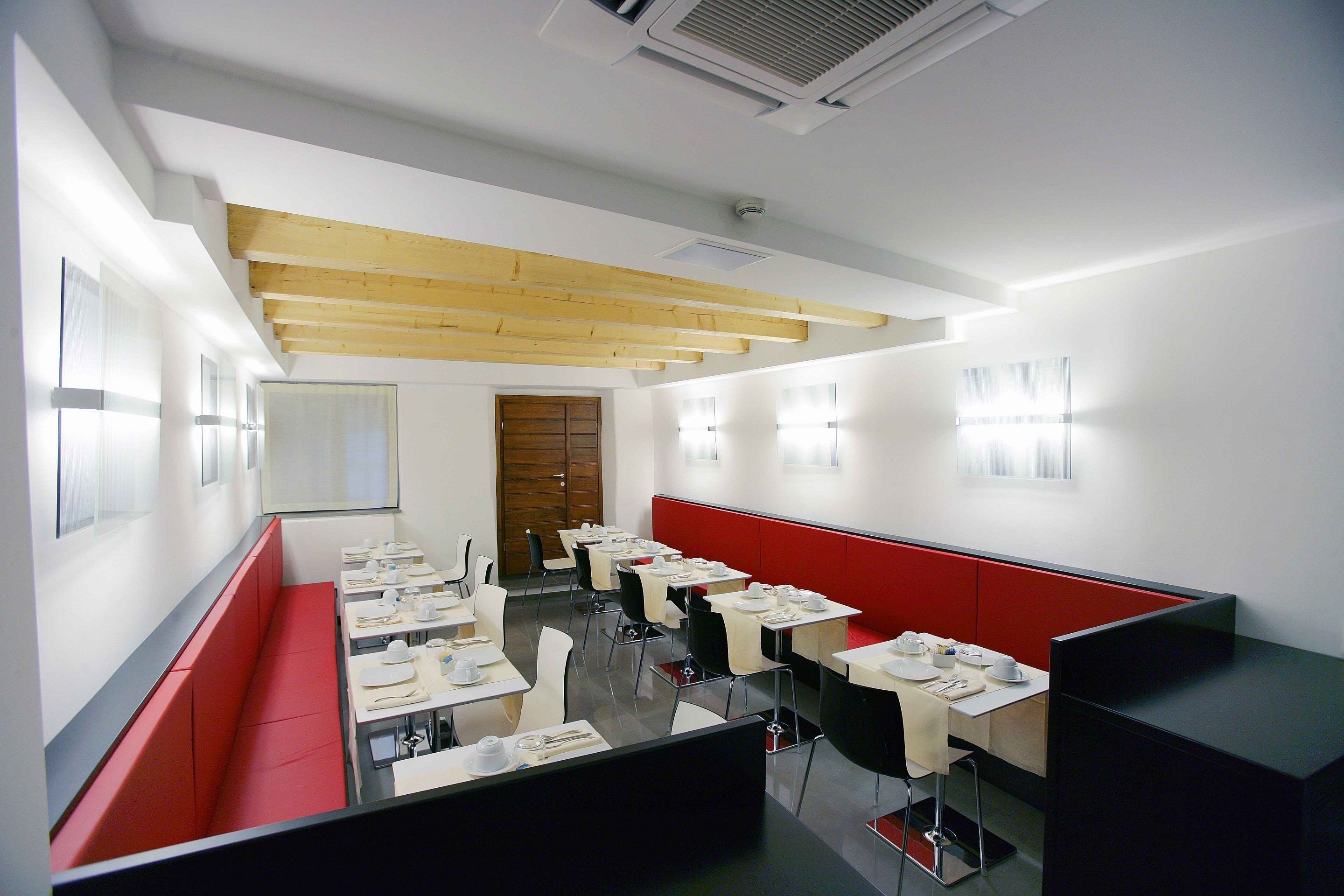 A modern dining area with booths and tables, wooden beams on the ceiling, and a red accent wall.