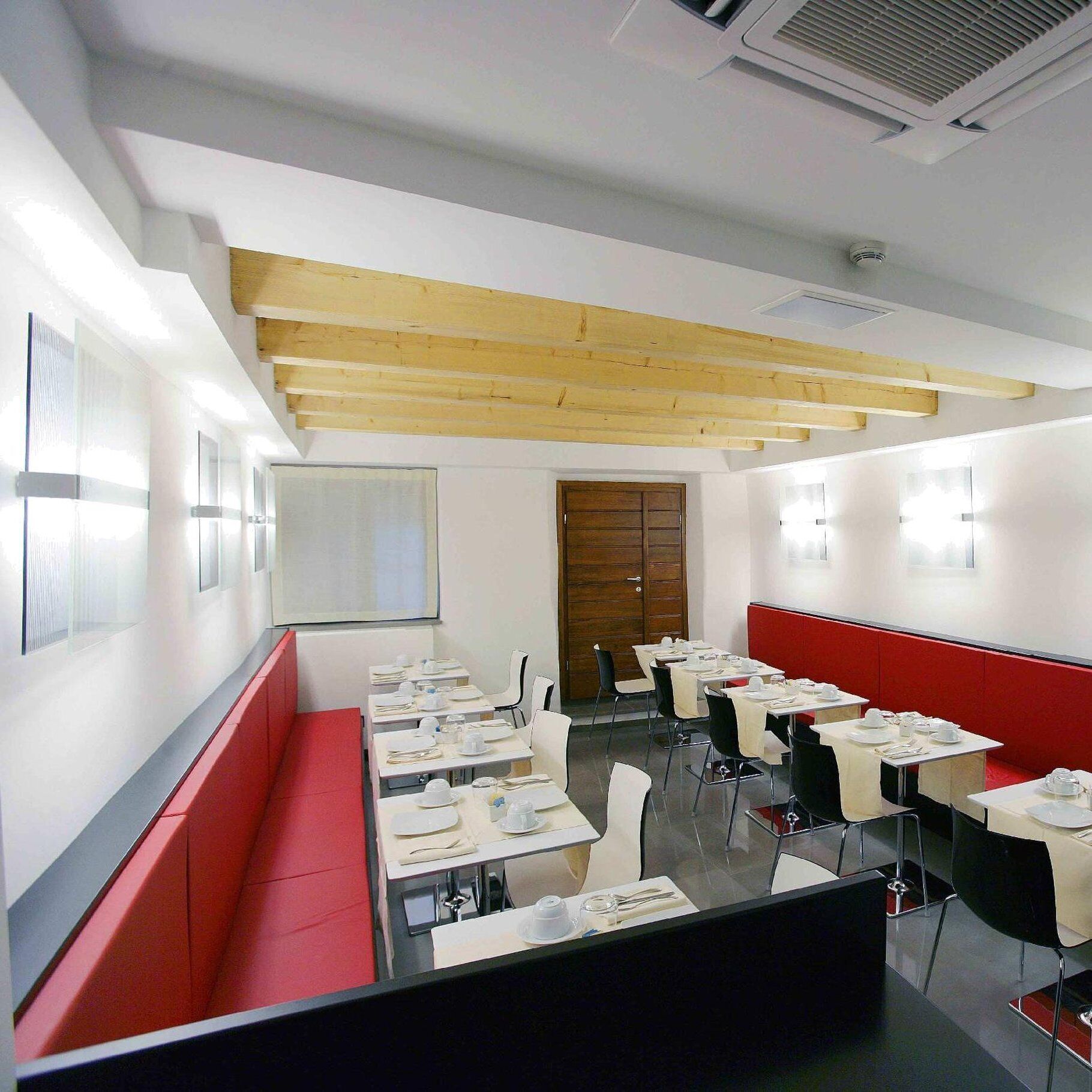 Un comedor moderno con mesas blancas, asientos tapizados en rojo y vigas de madera en el techo.