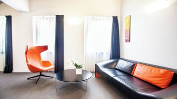 A modern living room with a leather sofa, an orange chair, a round coffee table, and large windows with curtains.