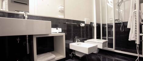 A modern bathroom with a black marble floor, a white sink, a glass shower enclosure, and a towel rack.