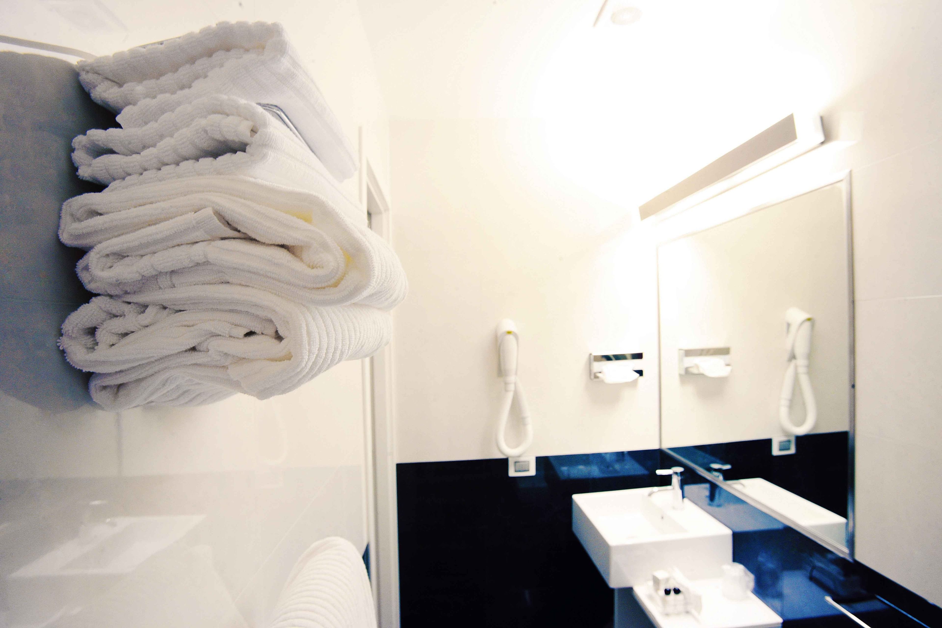 A bathroom with a stack of white towels, a white sink, and a mirror.