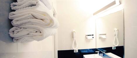 A bathroom with a stack of white towels, a white sink, and a mirror.