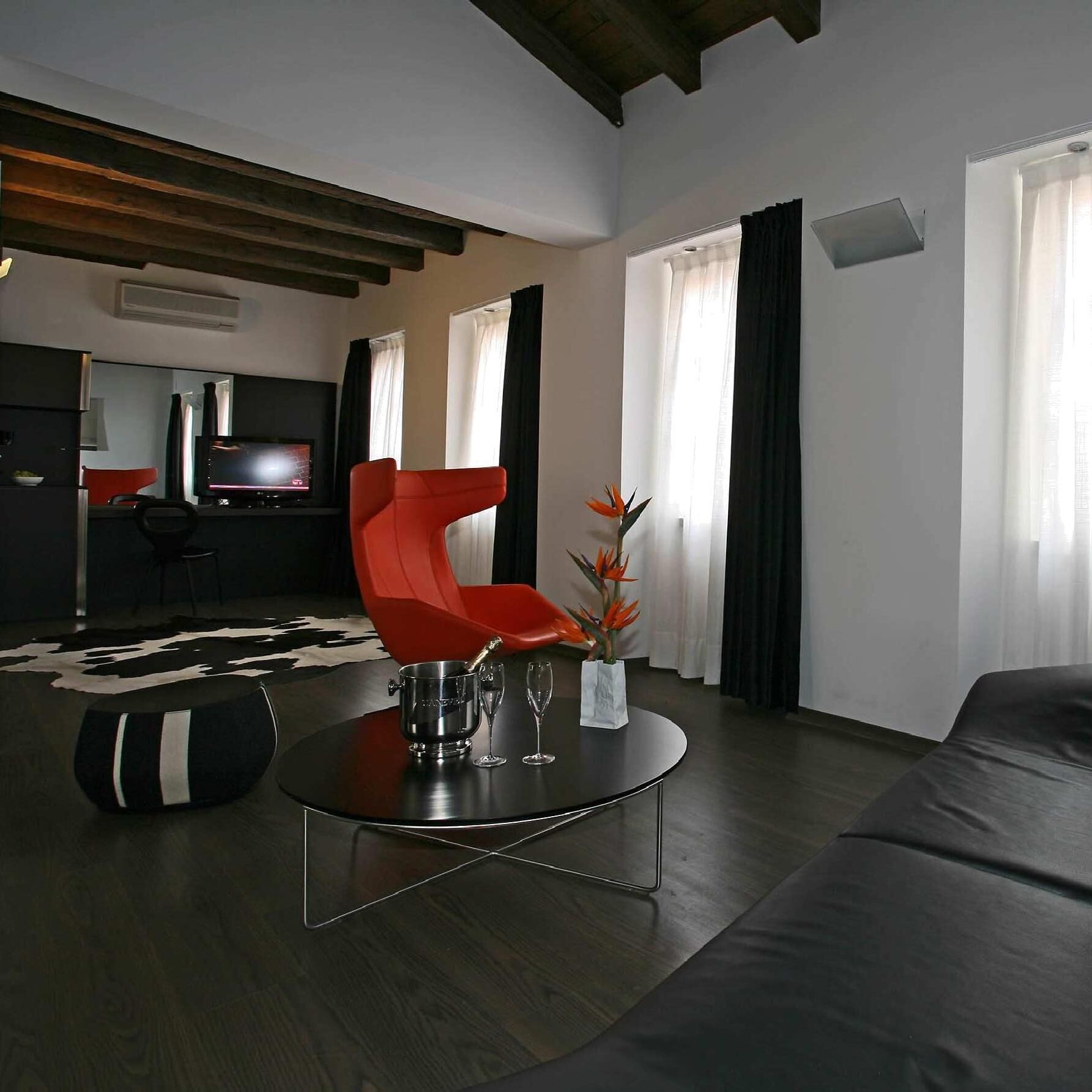 A modern living room with a red chair, a round coffee table, and a sofa. There is a flat-screen TV and a dining area in the background.