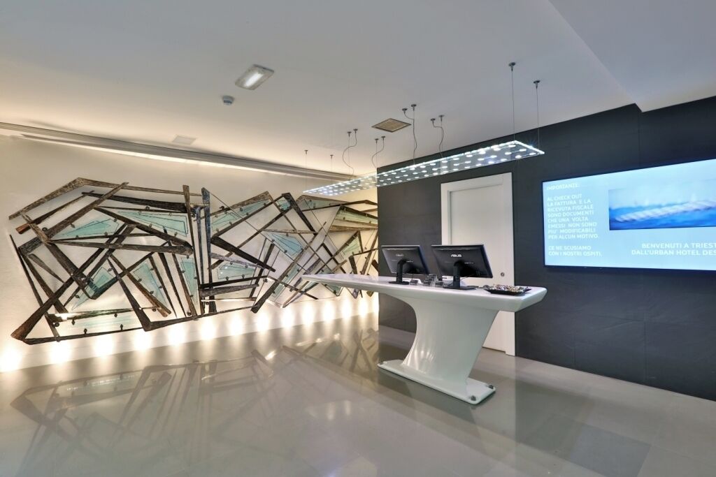 Una moderna area reception con un'installazione di vetro soffiato, una scrivania reception e un display digitale.