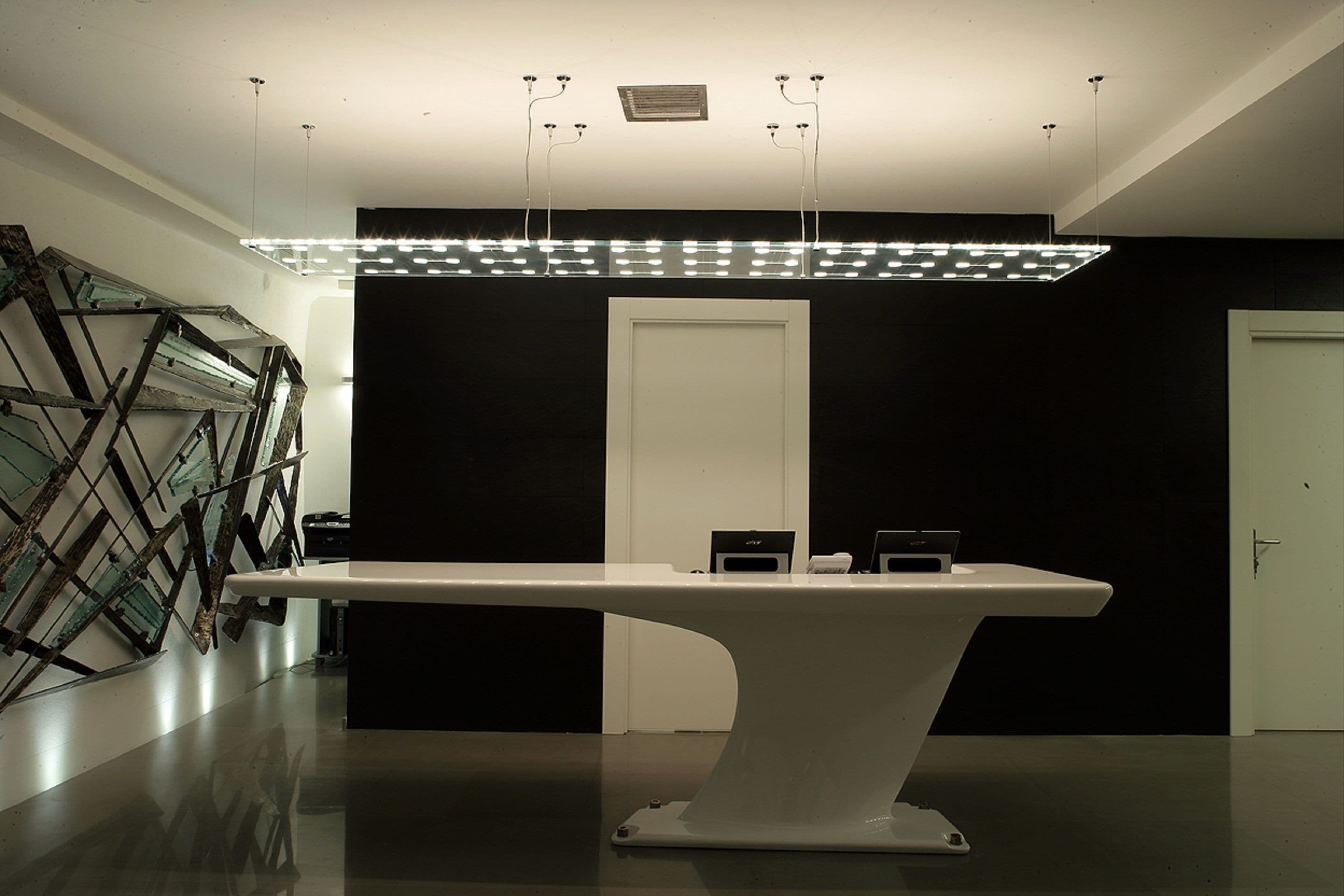Un interior moderno con una mesa central, paredes negras y una escultura de vidrio a la izquierda.