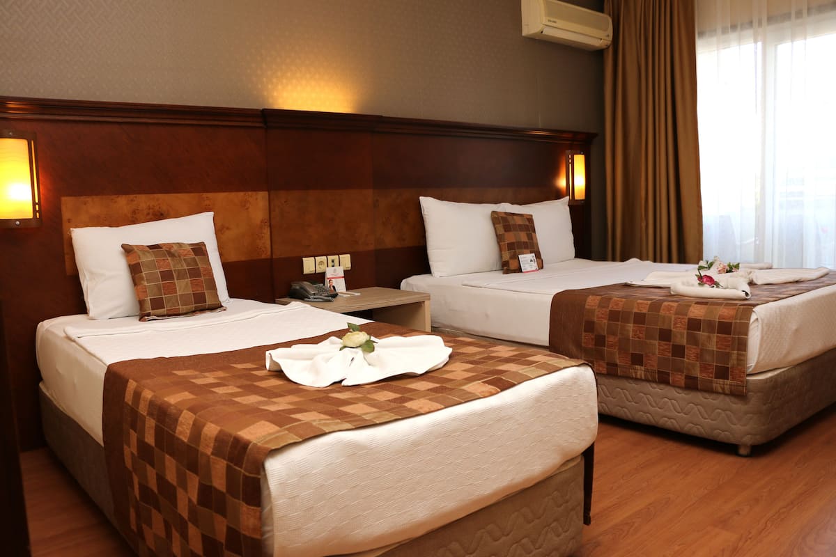 A hotel room with two beds, each with a brown checkered bedspread, white pillows, and a white towel on the beds. There is a wooden headboard, a nightstand with a lamp, and a window with curtains.