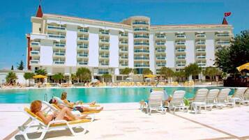 A hotel with multiple balconies overlooking a swimming pool, surrounded by sun loungers and umbrellas.