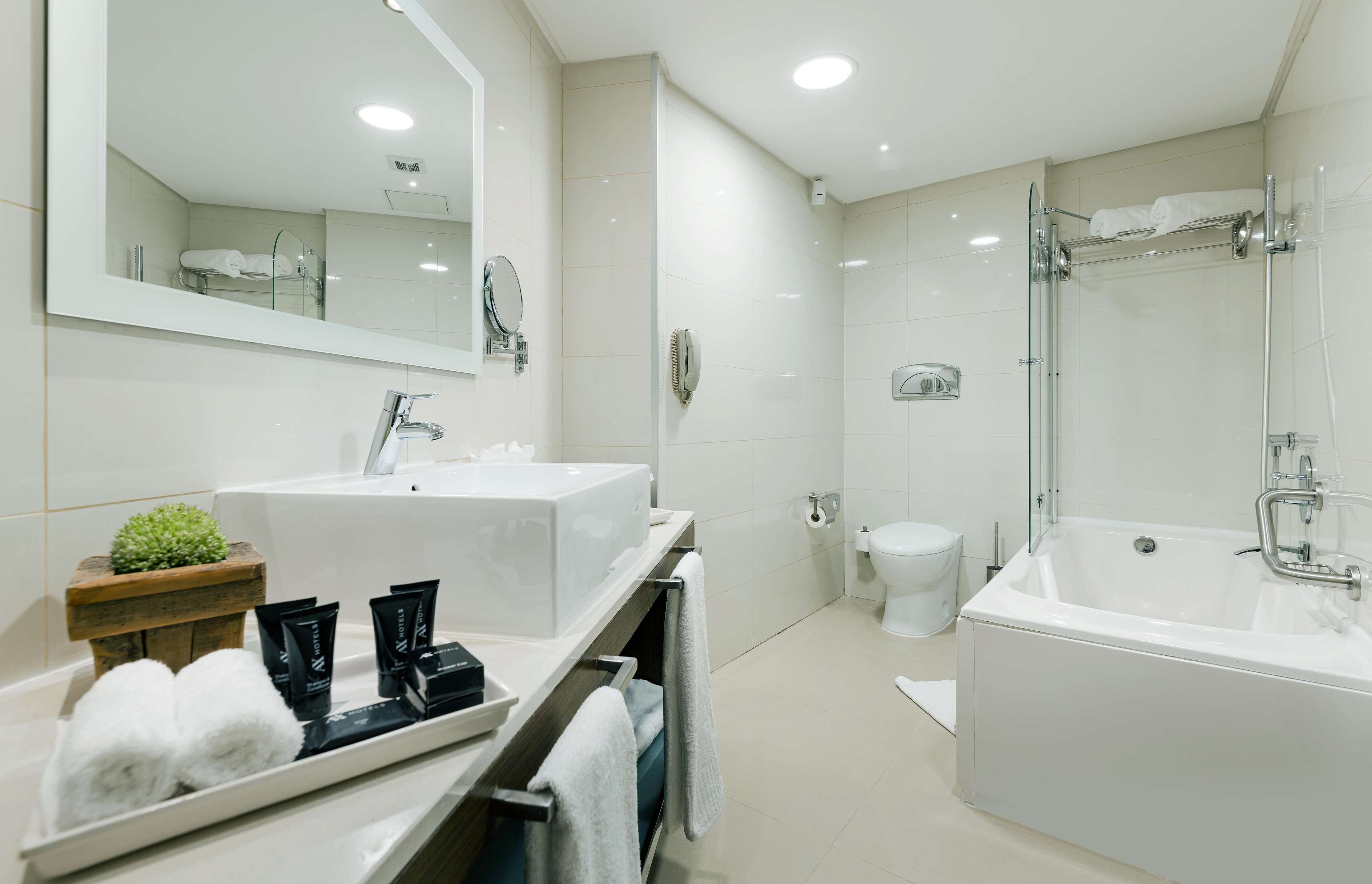 A modern bathroom with a large mirror, two sinks, a bathtub, and a toilet.