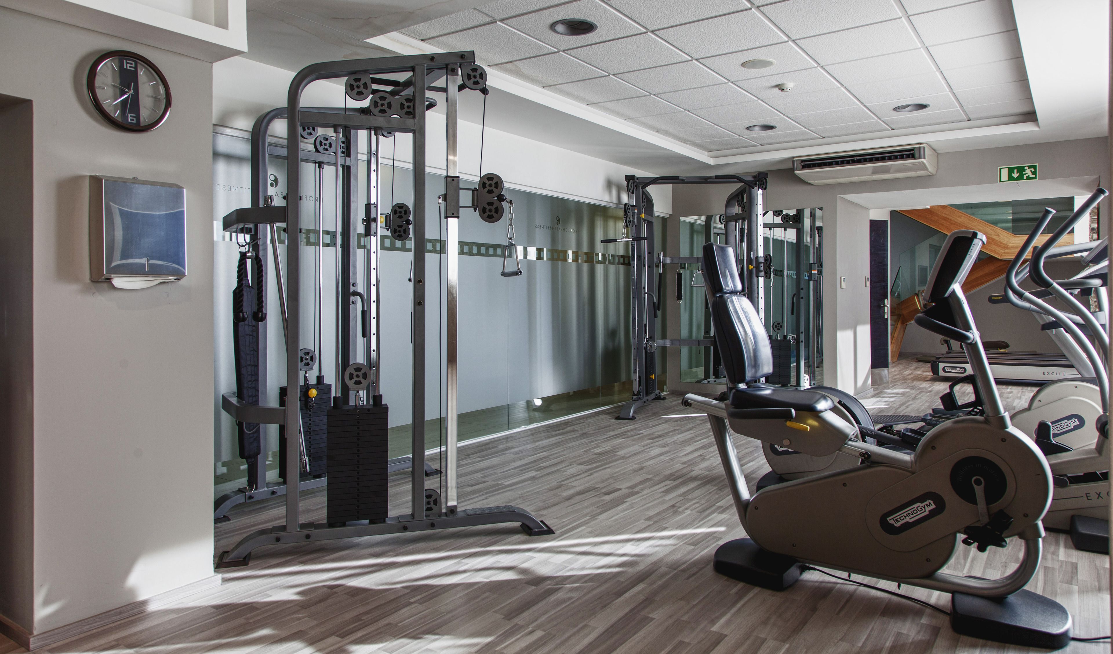 Ein Fitnessstudio mit Laufbändern, Krafttrainingsgeräten und einer Spiegelwand.