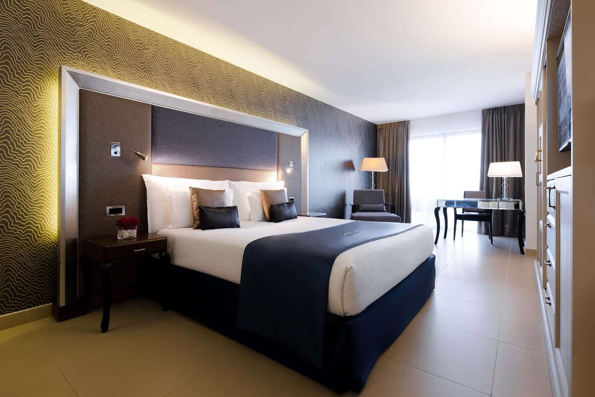A hotel room with a large bed, bedside tables, a desk, and a chair.