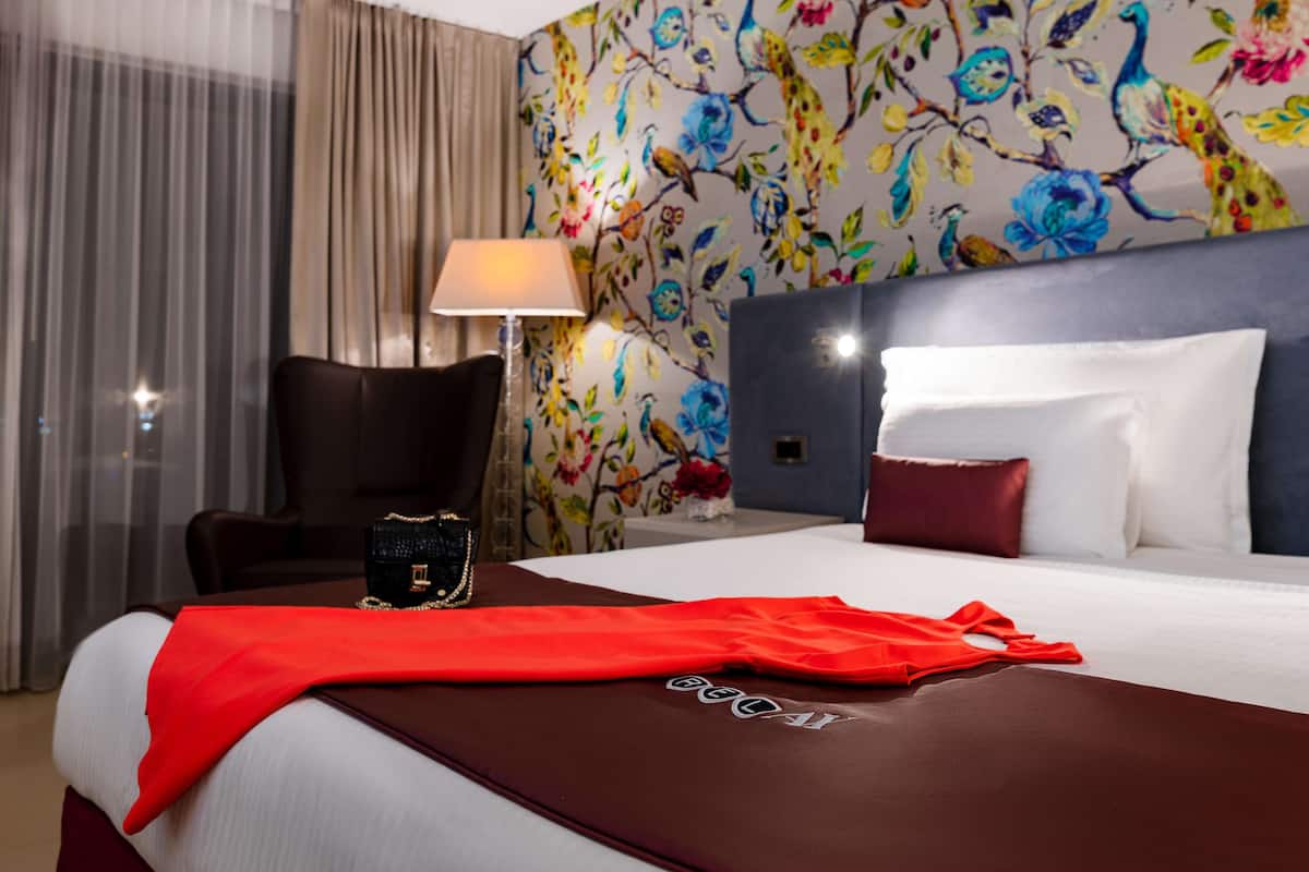 A hotel room with a bed, a chair, a lamp, and a floral wallpaper.