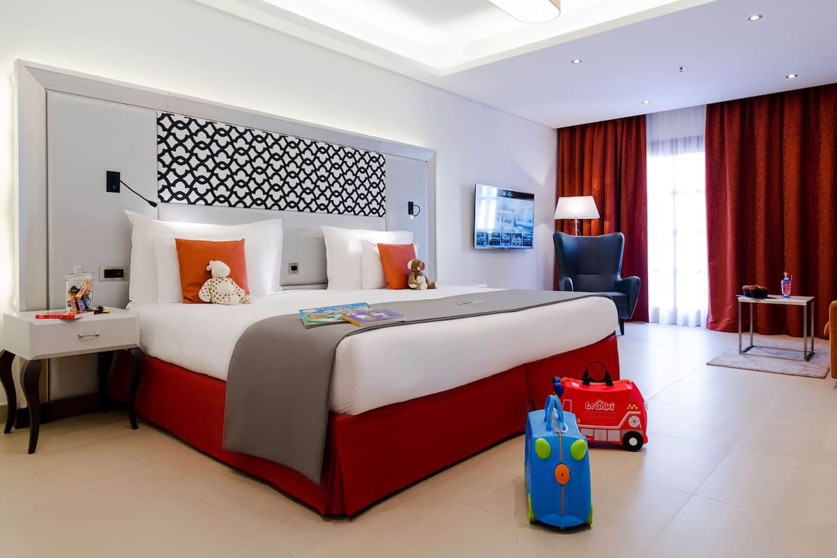 A modern hotel room with a large bed, a desk, a TV, and a red curtain.