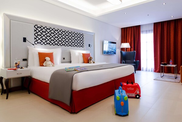 Una habitación de hotel moderna con una cama grande, un escritorio, un televisor y una cortina roja.