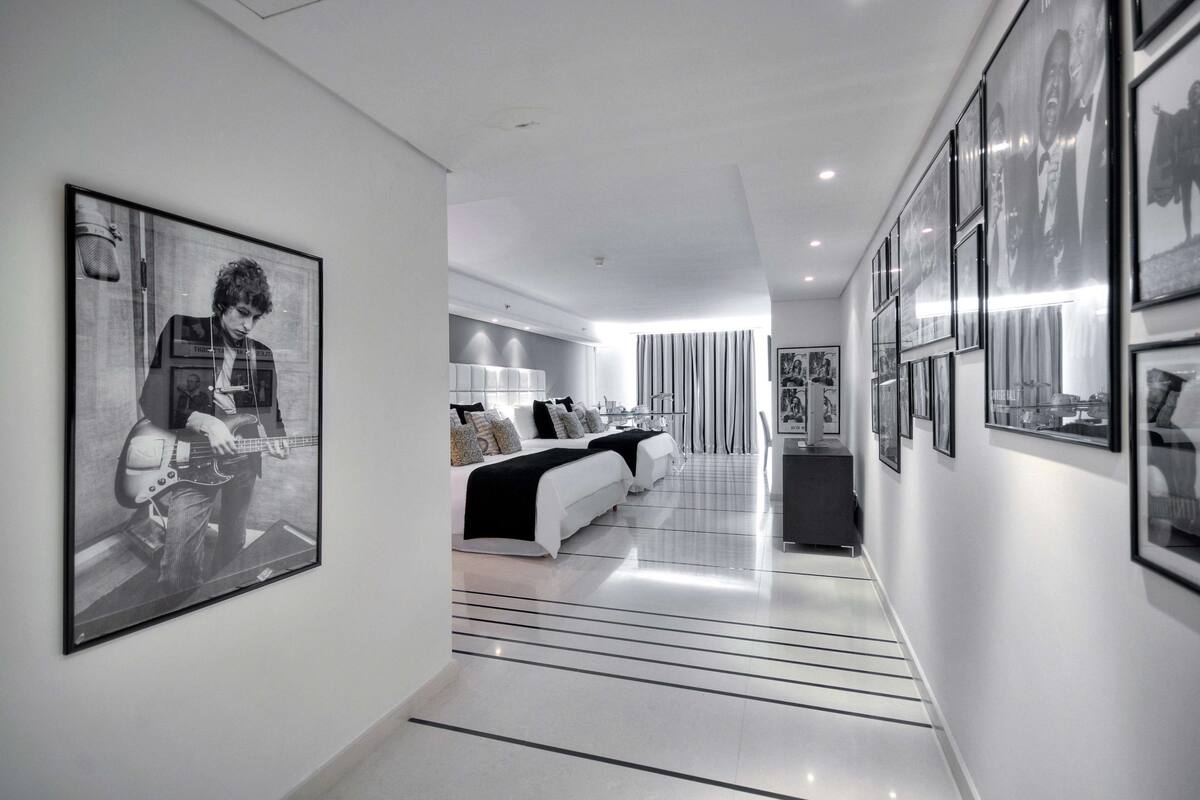A modern hotel corridor with framed artwork on the walls, a central seating area with a sofa and lamps, and a clean, minimalist design.