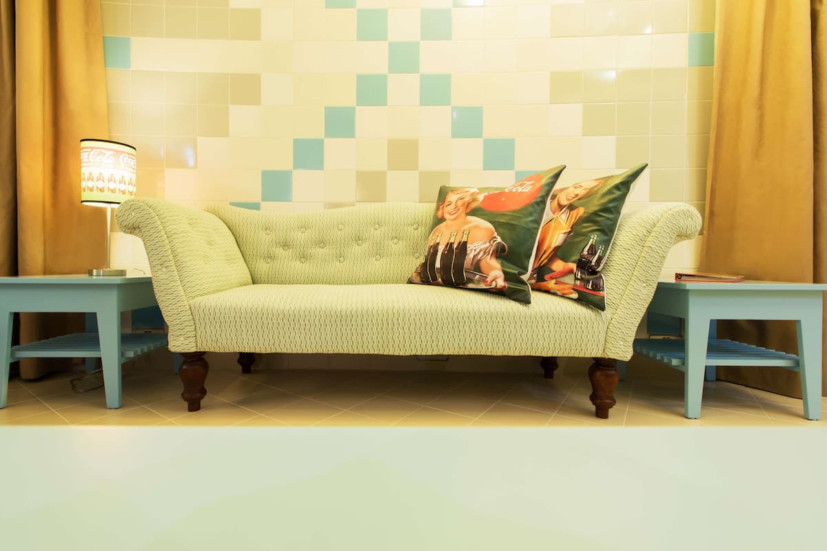 A sofa with two pillows, a lamp, and two side tables in a room with tiled walls.