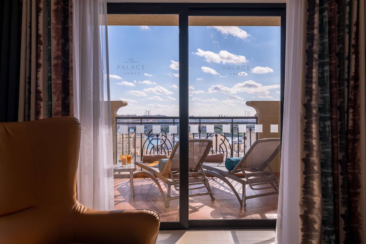 A balcony with a view of the city, furnished with chairs and a table, and curtains on the sides.
