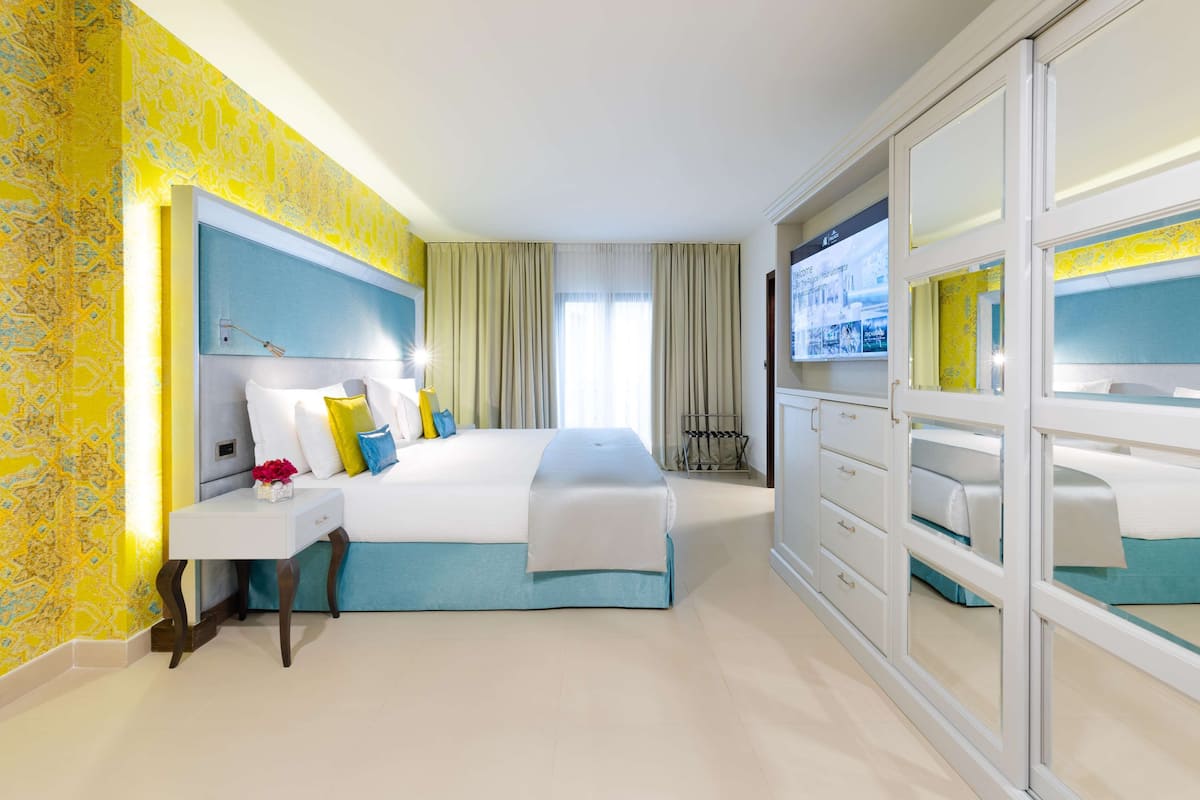A hotel room with a large bed, a bedside table, a wardrobe, and a view of the city through the window.