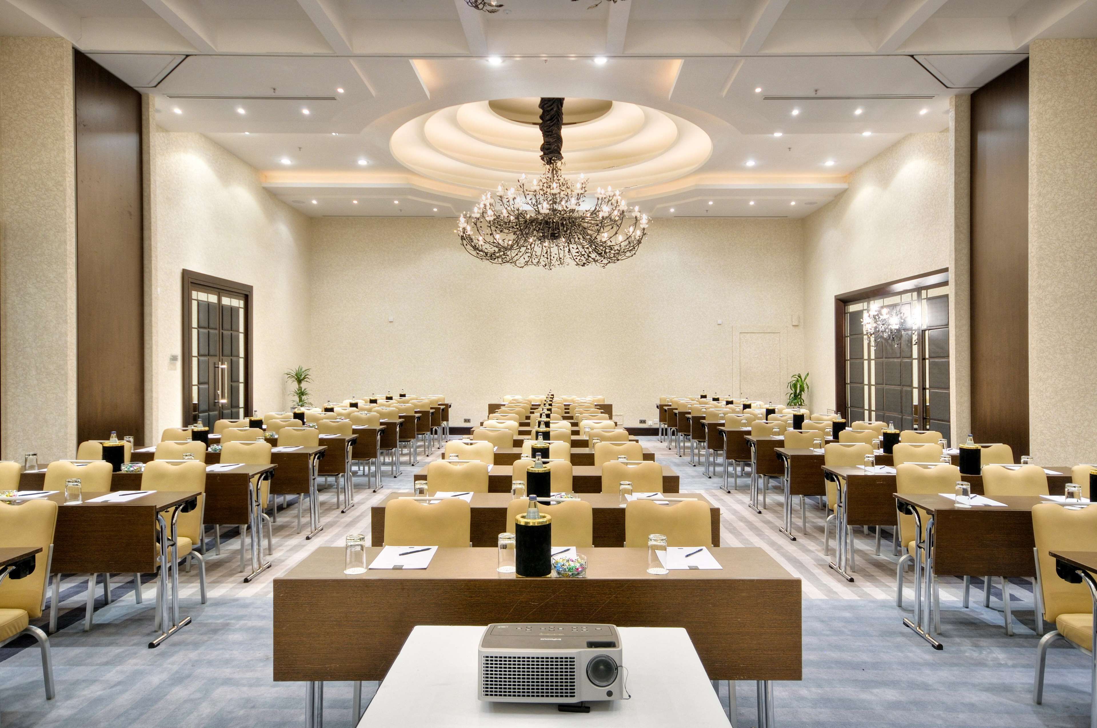 A conference room with rows of tables and chairs, a chandelier, and a projector at the front.