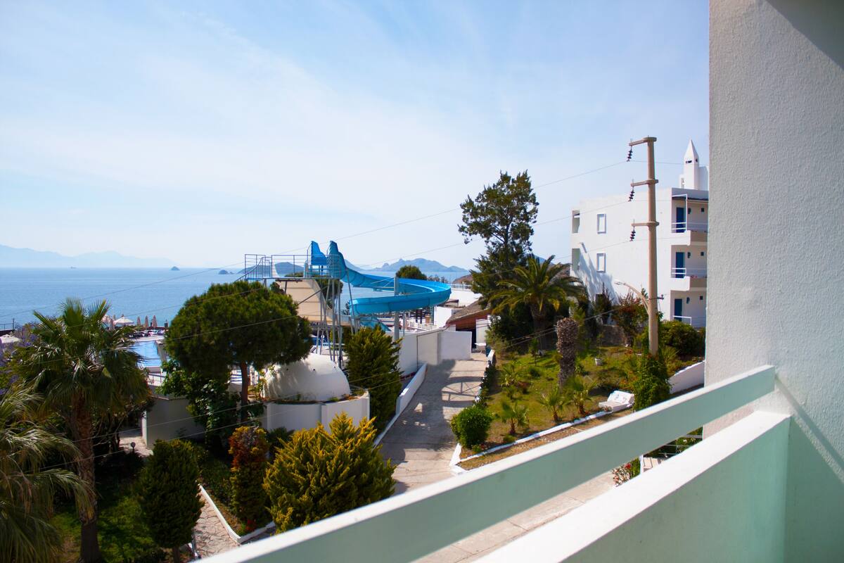 A coastal resort with a pool, palm trees, and a blue water slide.