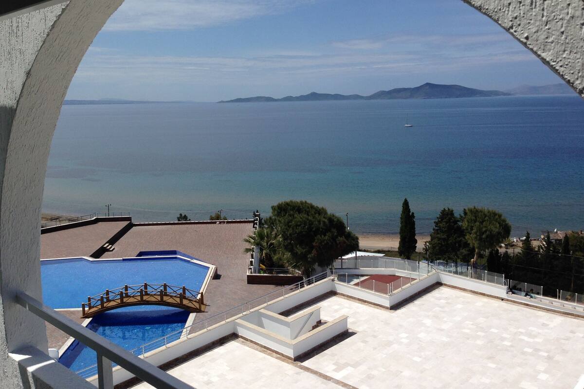 A pool area with a bridge, a beach, and a view of the sea and distant islands.