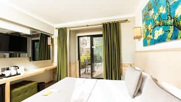 Une chambre d’hôtel comprenant un lit, un bureau avec un téléviseur à écran plat, une petite table avec une bouilloire et des tasses, et un tableau accroché au mur.