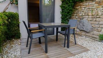 An outdoor patio with a table and chairs, a stone wall, and a wooden deck.