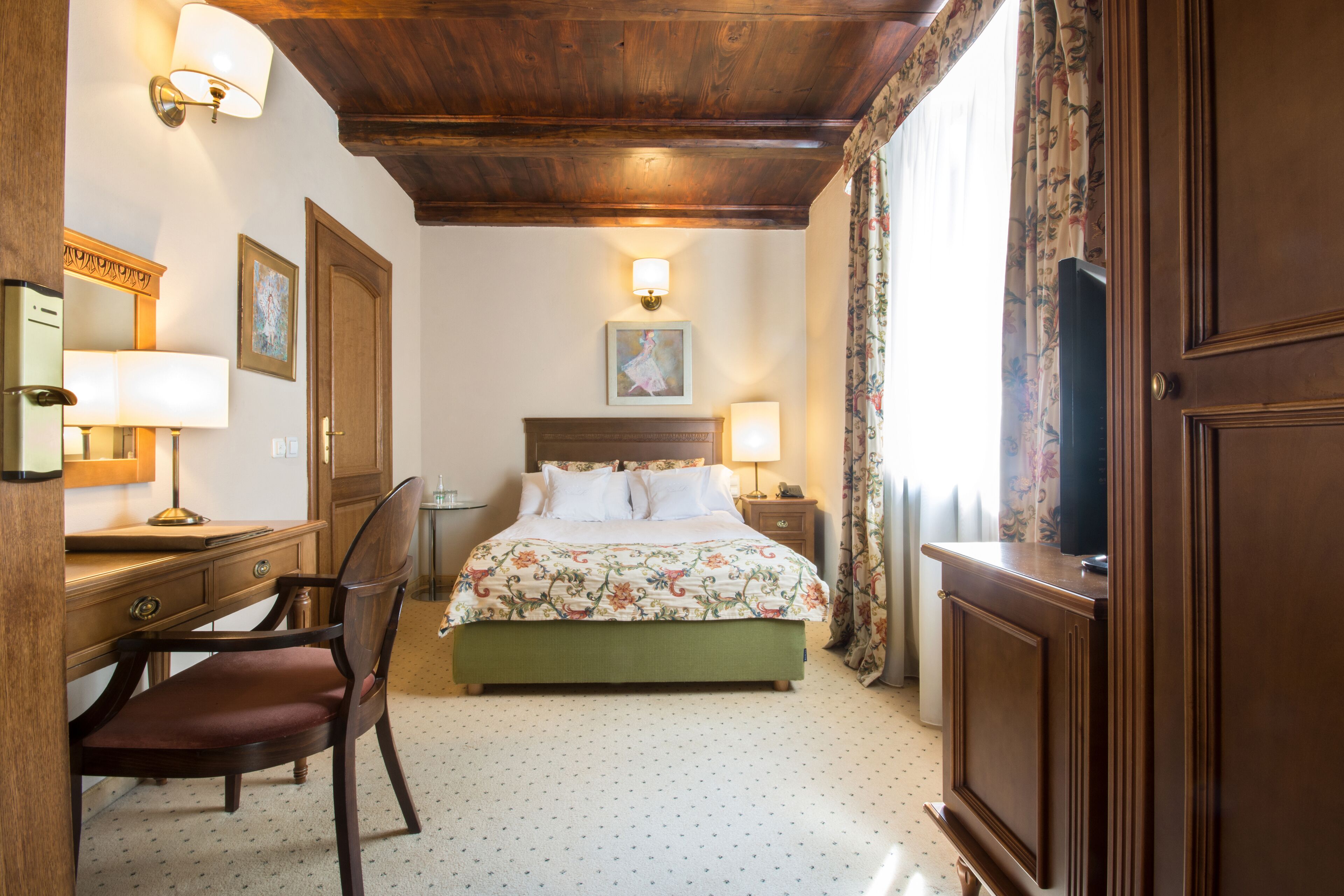 Une chambre d’hôtel comprenant un lit, un bureau avec une chaise, une commode et une table de chevet avec une lampe.