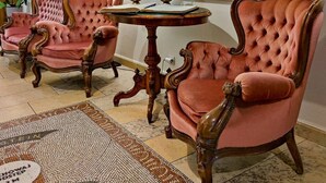 A room with antique-style furniture, including two pink upholstered chairs and a table, a large painting on the wall, and a tiled floor with a mosaic pattern. - Hotel Rubinstein (Kraków)