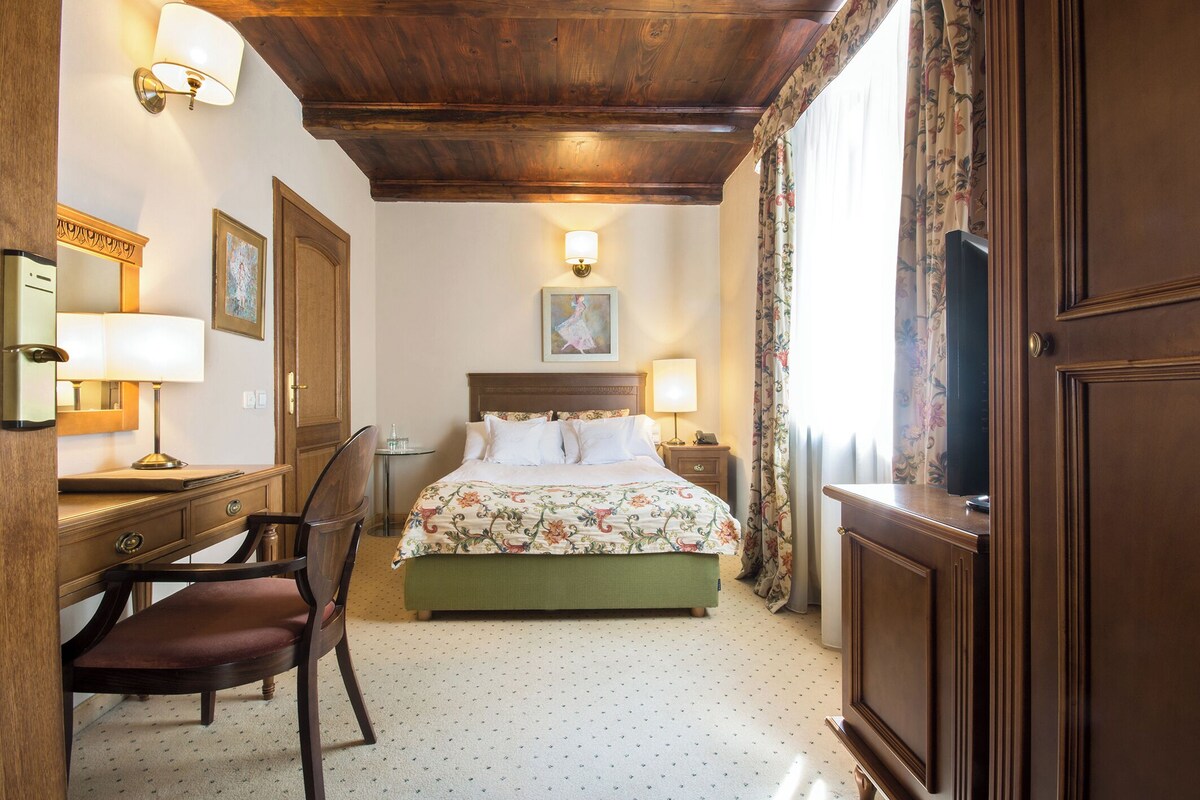 A hotel room with a bed, desk, chair, and a wooden ceiling.