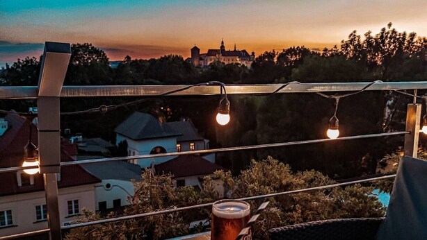 A balcony with a table set for two, featuring a cocktail and a menu. - Hotel Rubinstein (Kraków)