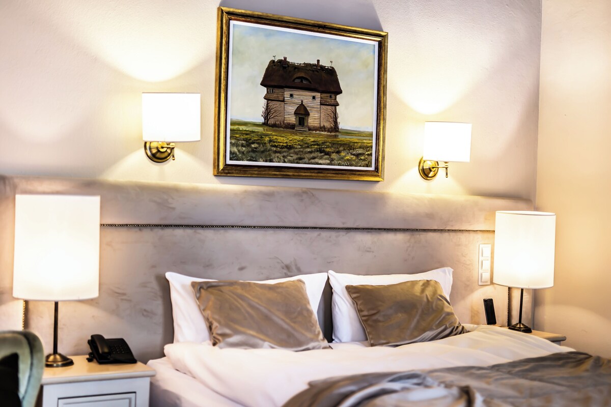 A hotel room with a bed, two bedside lamps, a telephone, and a framed picture on the wall.