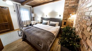 A bedroom with a wooden ceiling, a brick wall, a bed with a grey blanket, bedside lamps, and a potted plant. - Hotel Rubinstein (Kraków)