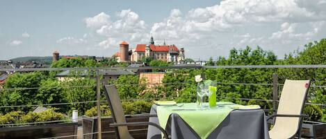 Una terraza con una mesa preparada para dos, con vista a un edificio histórico de techo rojo.