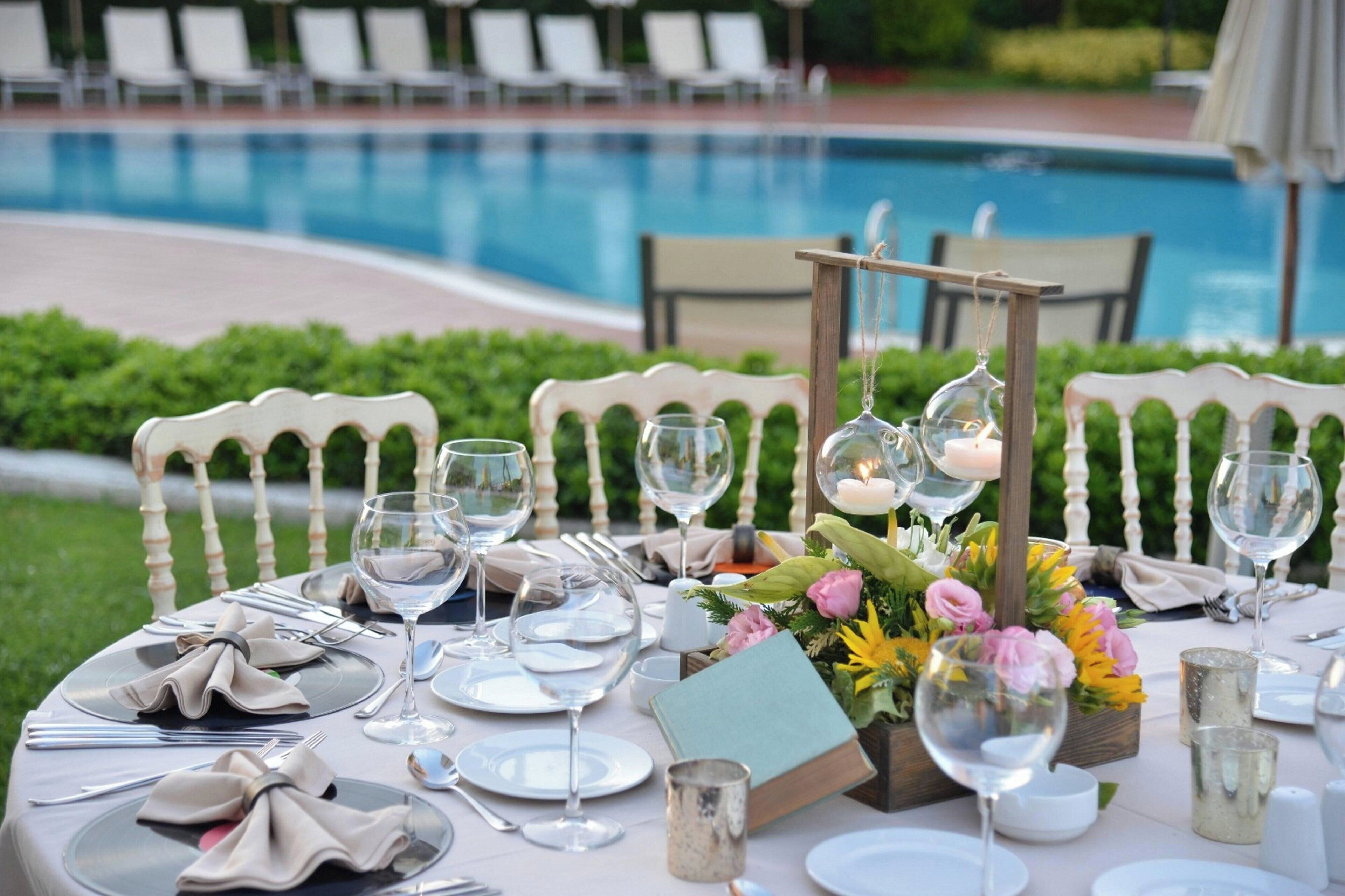 Ein Tisch ist festlich für ein Essen im Freien gedeckt, im Hintergrund ist ein Pool zu sehen.