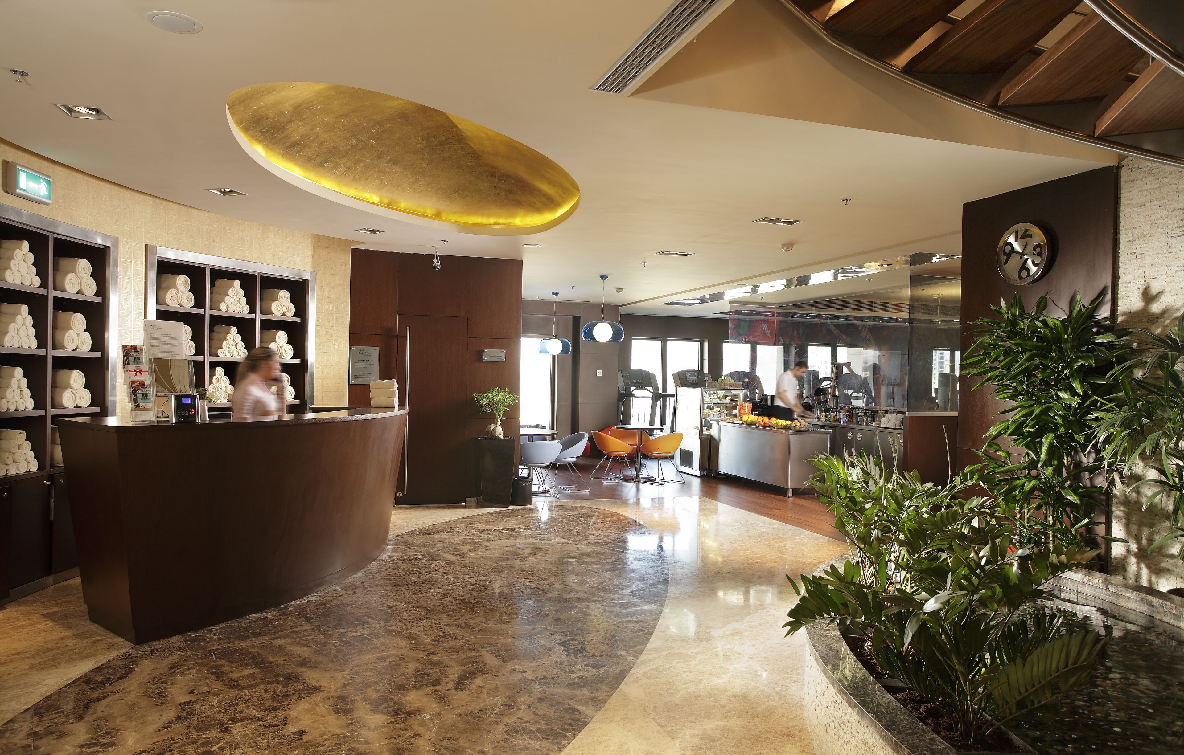 A modern hotel lobby with a reception desk, seating area, and a large clock on the wall.