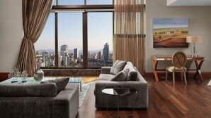 A modern living room with a city view, a sofa, a coffee table, and a desk with a chair.
