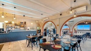 A spacious restaurant with high ceilings, exposed beams, and a long counter with shelves of bottles. Tables are set with place settings, and the room has a modern, industrial design. - Ippotur Medieval Resort (Castelnuovo Magra)